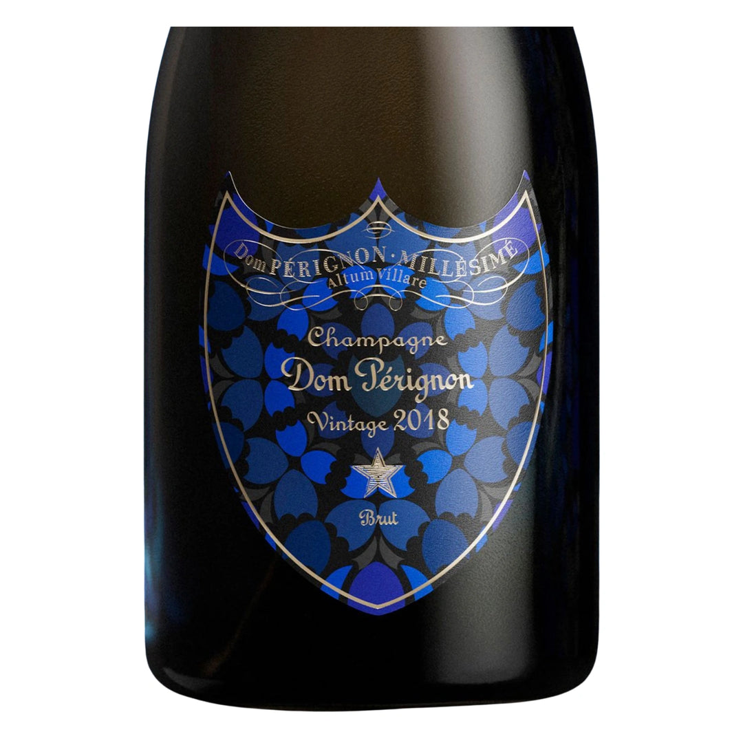 A bottle of Dom Pérignon Limited Edition Damien Hirst Brut 2018, featuring a prominent blue and black shield-shaped label with gold foil details on a white background.