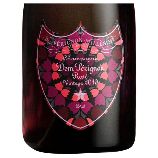 A close-up of a dark glass bottle of Dom Pérignon Rosé Vintage 2010 Champagne, showing the iconic shield-shaped vintage label with pink, red, and black rose patterns.